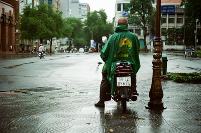 穿绿色连帽衫的男子白天骑红色摩托车上路
